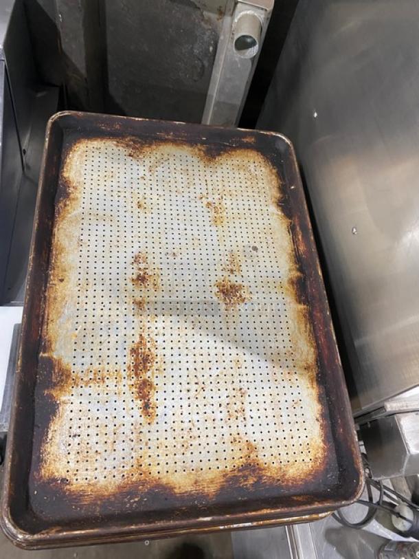 Commercial perforated sheet pan, shows signs of heavy use and rust, ideal for enhancing airflow in baking.