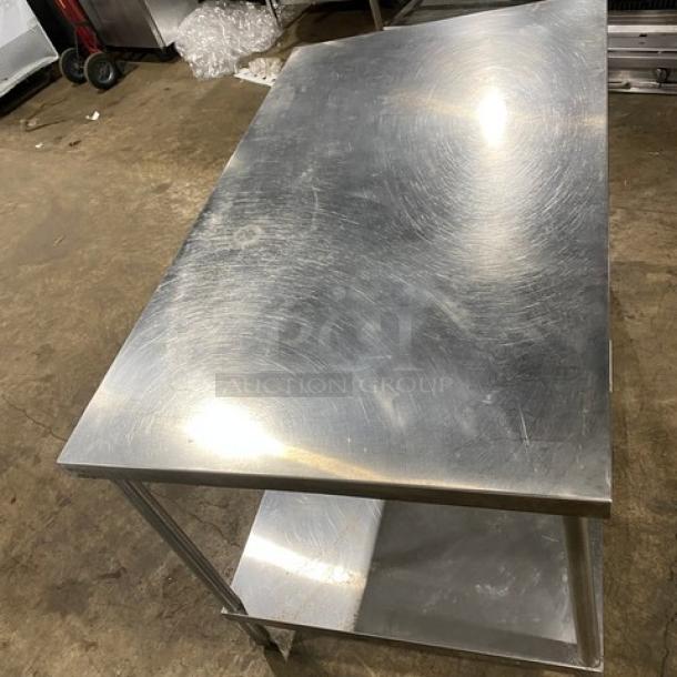 Commercial stainless steel single undershelf equipment stand on legs, showing wear; durable for kitchen or industrial use.