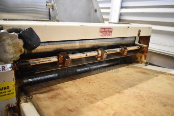 Moline commercial floor-style dough sheeter with casters, 125 volts, 1 phase. Visible wear and rust on rollers and frame.