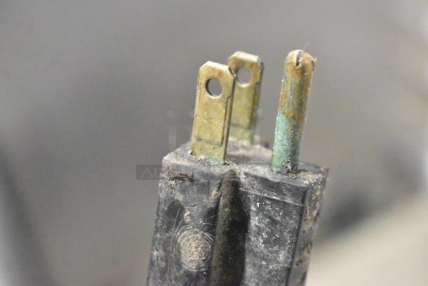 A close-up image of a worn and tarnished electrical plug with visible wear and corrosion on the prongs.