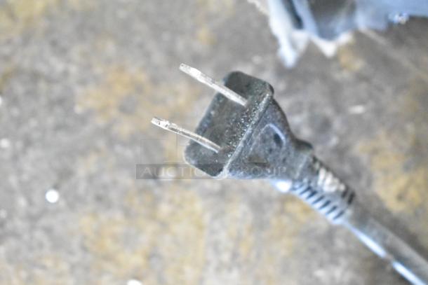 Close-up of a worn two-prong power plug on a television cord, resting on a textured surface.