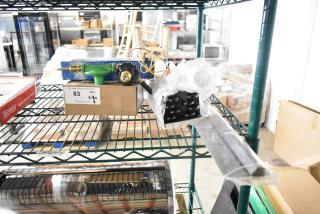 Eight brand new scratch and dent items including Delfield coil evaporator and Watts safety relief valve on shelf with auction tag.