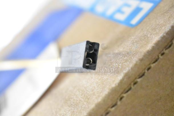 Close-up of a new connector and wire on a cardboard surface, part of an auction lot including Delfield coil evaporator and Watts valve.