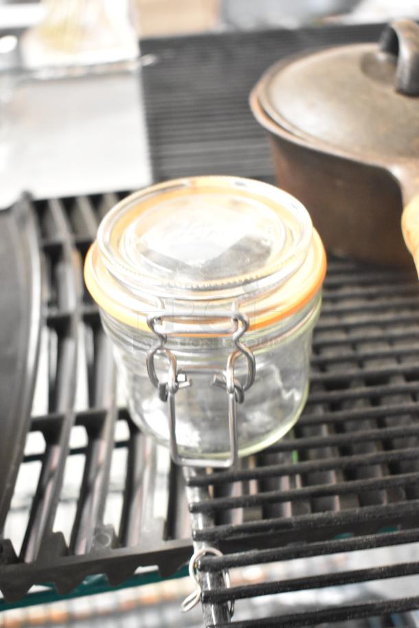 Glass jar with orange seal and metal clasp on a black metal shelf; part of a six-item lot including a blade sharpener.