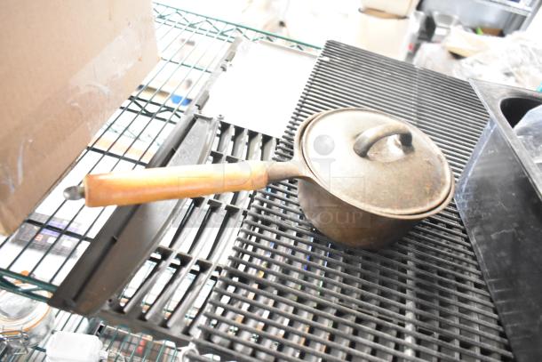 Antique metal saucepan with wooden handle on a rack, part of a lot including a jar, blade sharpener, bin, and ice vent cover.
