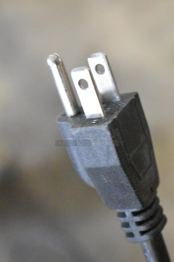 Close-up of a three-prong electrical plug with a black plastic casing, showing minor wear.