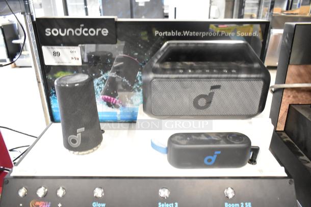 Two store display speakers: Soundcore portable waterproof speakers, visible logo and branding, modern design, like new condition.