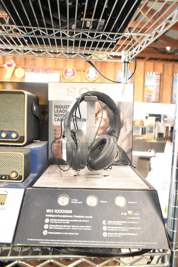 Sony WH-1000XM4 headphones on store display, featuring noise cancellation. Surrounding Skull Candy and Onn speakers.