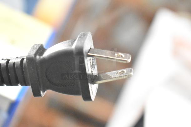 Close-up of a black electrical plug with visible metal prongs. Background is blurred and indistinct.