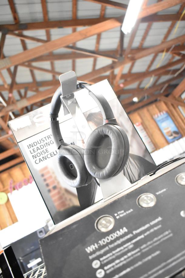 Sony WH-1000XM4 headphones display with noise-canceling feature showcased in store. Includes display stand and branding.