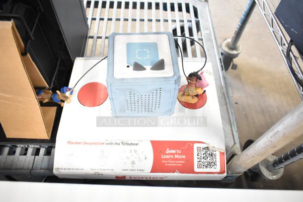 TonieBox store display with blue speaker cube, figurines, and promotional signage. Includes QR code for more info.