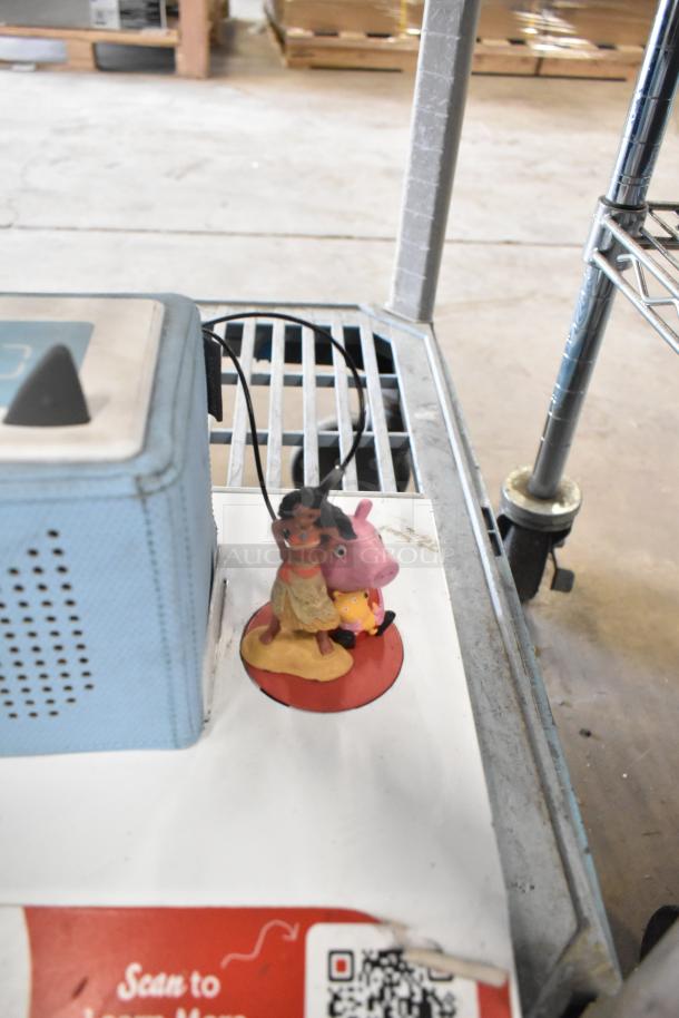 Three store displays featuring a blue TonieBox 1 and figurines on a metal shelf, including QR code and product graphics.