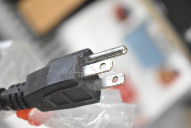 Close-up of a black three-prong electrical plug, part of an auction lot including TonieBox, JBL, and Altec speakers.