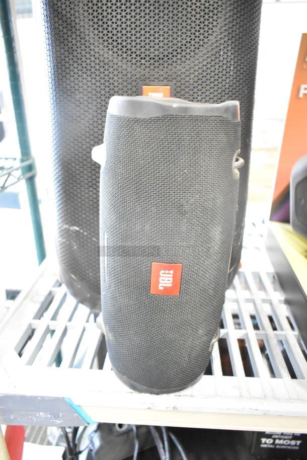 Three speakers including two JBL models and one Altec, featuring black mesh design, in used condition on a display shelf.