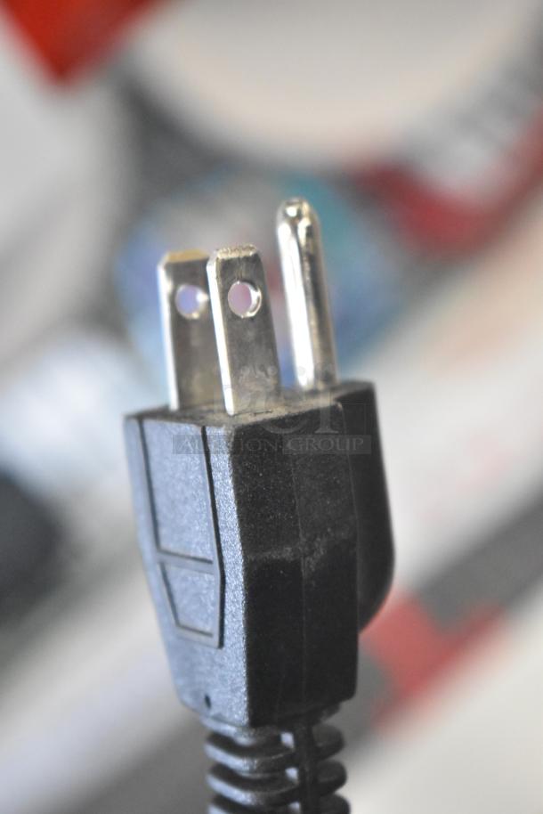 Close-up of a black power plug with two prongs, part of an auction item package including TonieBox 2s, Turtle Beach headphones, and a Sonos sound bar.