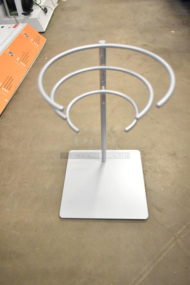 Silver metal stand with three circular tiers on a square base, shown on a concrete floor.