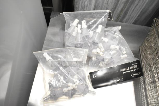 32 brand new scratch and dent kitchen items including Acopa liquor pourers, packaged. Multiple items visible on a stainless steel surface.