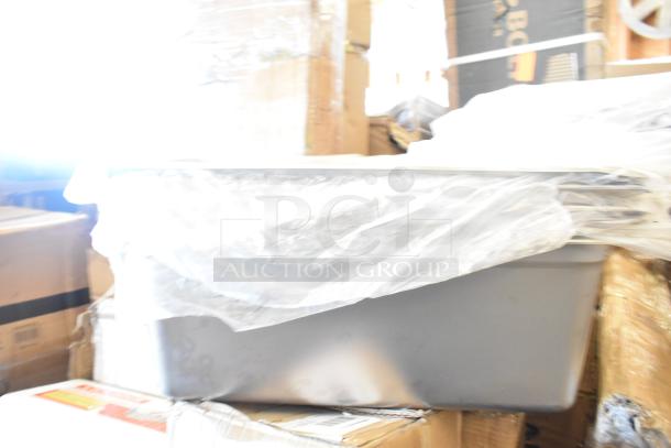 18 brand new scratch and dent items stacked with plastic wrap, including visible boxes. Auction lot includes fry pot, high chair, drum caddy.