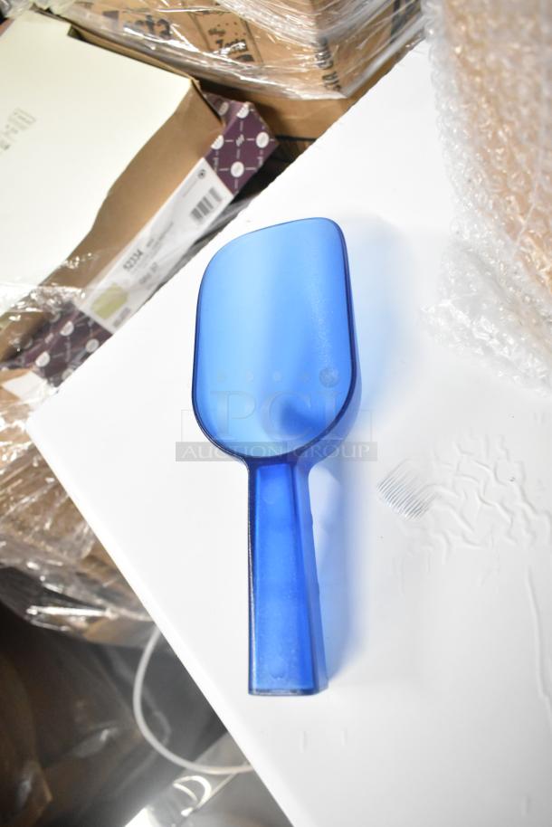 Blue ice scoop on a white surface near cardboard boxes, part of Scotsman UN0815AX-1A ice machine package.