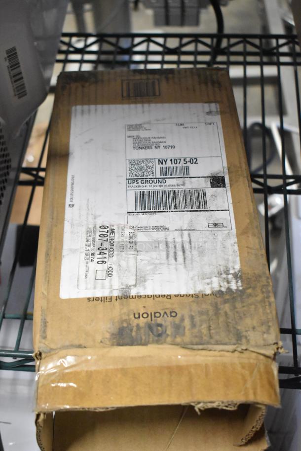 Cardboard box on metal shelf, packaging label visible, labeled for UPS ground shipment. Box shows wear, marked "avalon."
