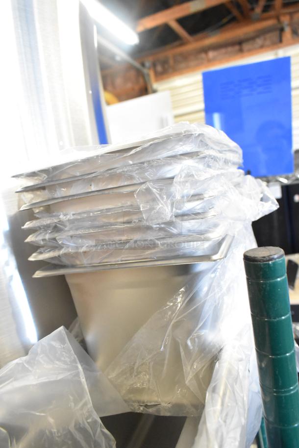 Stack of brand new stainless steel drop-in bins wrapped in plastic, with visible scratch and dent marks.