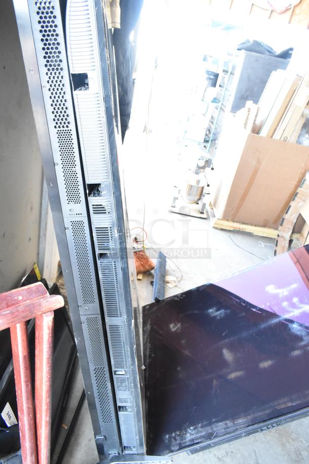 Four televisions including Samsung QN77S90FDF 77", Samsung UN75U7900FD 75", and Vizio models, stacked in storage.