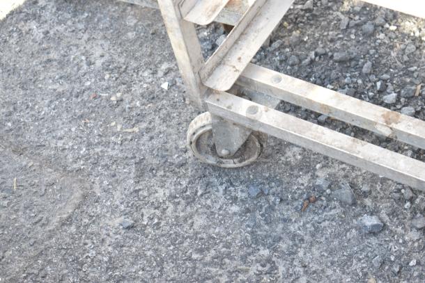 Channel metal pan rack on commercial casters, shown on a rough surface. Rust visible, suggesting used condition.