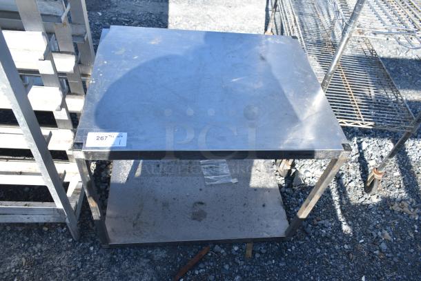 Commercial table with metal under shelf, visible wear, sturdy metal frame. Tag reads "267." Ideal for industrial use.