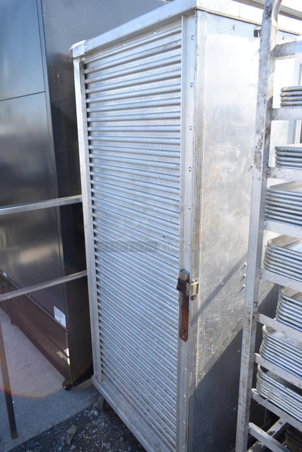 Commercial enclosed pan rack with metal door, on heavy-duty casters, showing signs of use; ideal for kitchen storage.