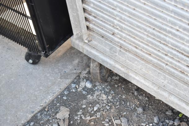 Commercial enclosed pan rack with heavy-duty casters, metal construction, and visible scuff marks, suitable for kitchen use.