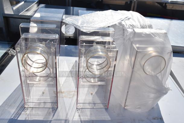 Three clear acrylic hoppers with circular metal rings, used condition, set on a white surface. Suitable for bid.