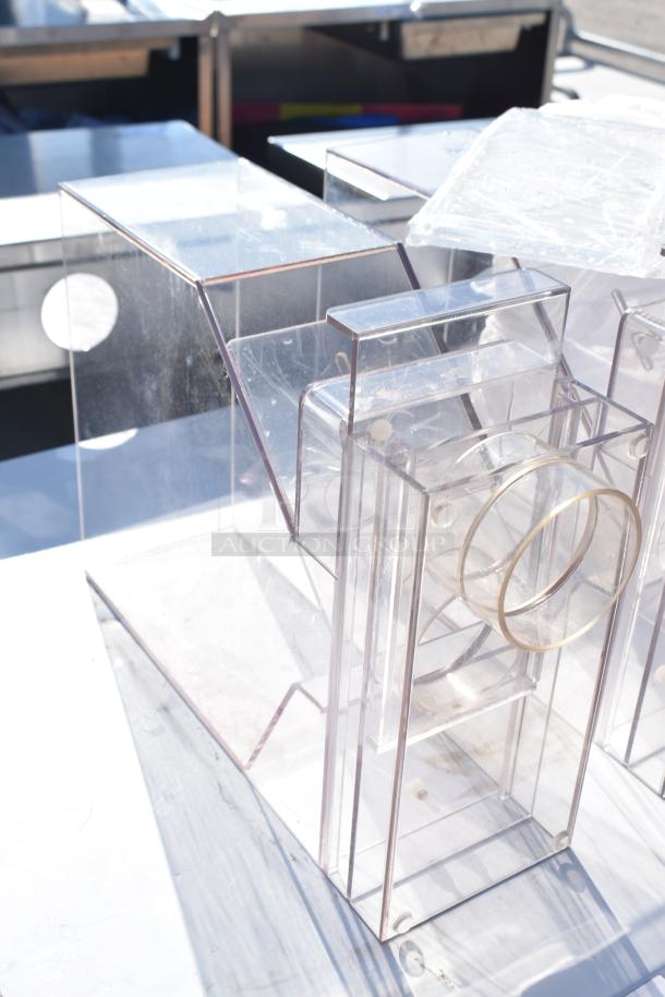 Three clear acrylic hoppers, in good condition, with cylindrical openings and stacking ability, ideal for bulk storage.