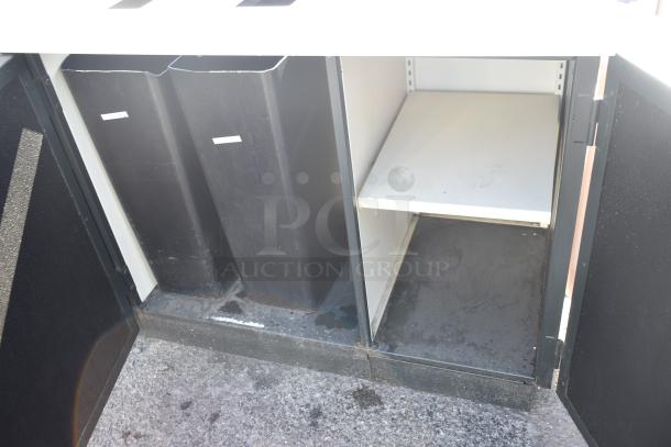 Trash can shell with dual trash deposit holes, featuring wooden doors. Includes empty bins and open shelving, in used condition.