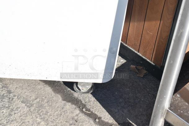 White poly ingredient bin with commercial casters, containing round cake pans. Visible wheels, used condition.