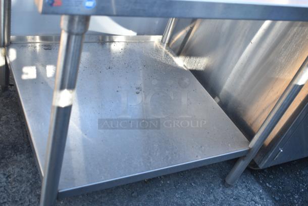 Stainless steel commercial table with under shelf, used condition, sturdy frame, some surface dirt present.