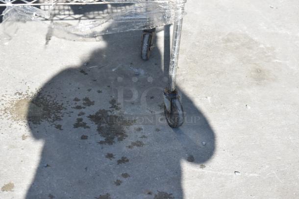 Chrome finish 4-tier wire shelving unit on commercial casters with contents. Shows one caster wheel, partially wrapped in plastic. Buyer must dismantle.