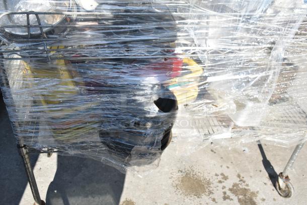 Chrome 4-tier wire shelving unit on commercial casters with contents, wrapped in plastic. Buyer must dismantle.