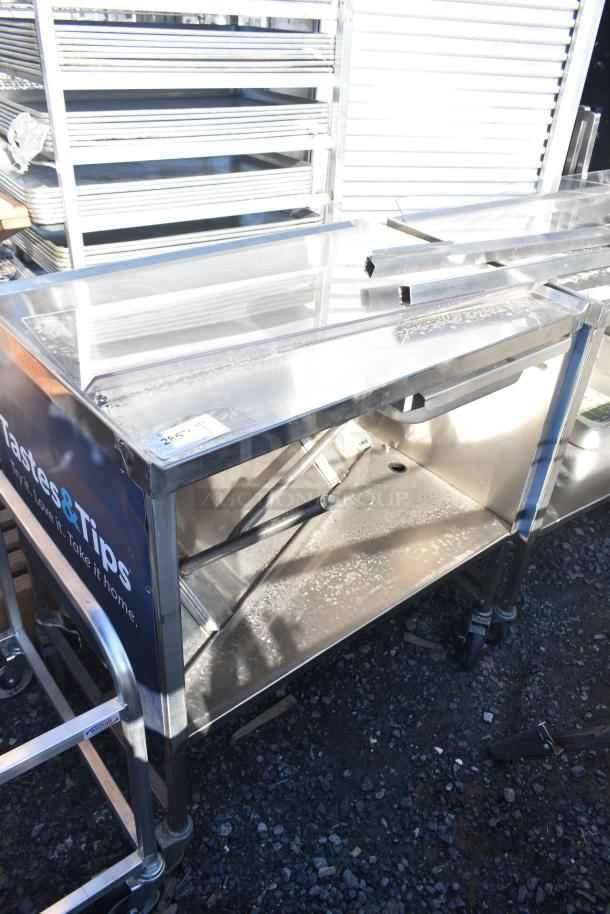 Commercial portable counter with under shelf and drawer on casters, metal frame, visible "Tastes & Tips" branding, used condition.