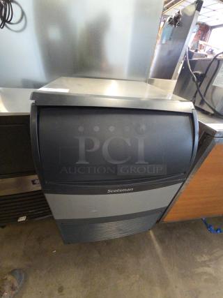 Scotsman undercounter ice maker, black and gray finish, stainless steel top, visible "Scotsman" label, commercial use.