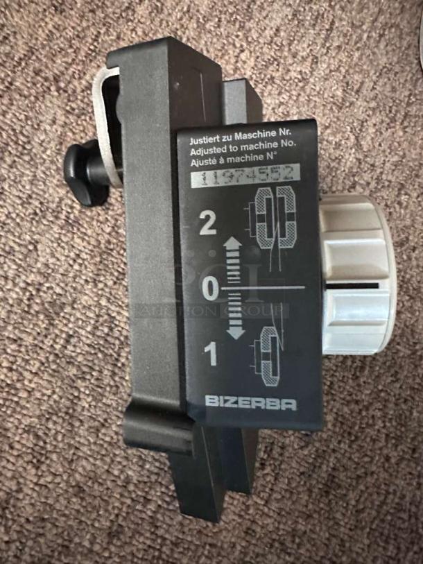 Close-up of a Bizerba GSP HD P-21 slicer adjustment knob with calibration markings and Bizerba logo, on carpeted surface.