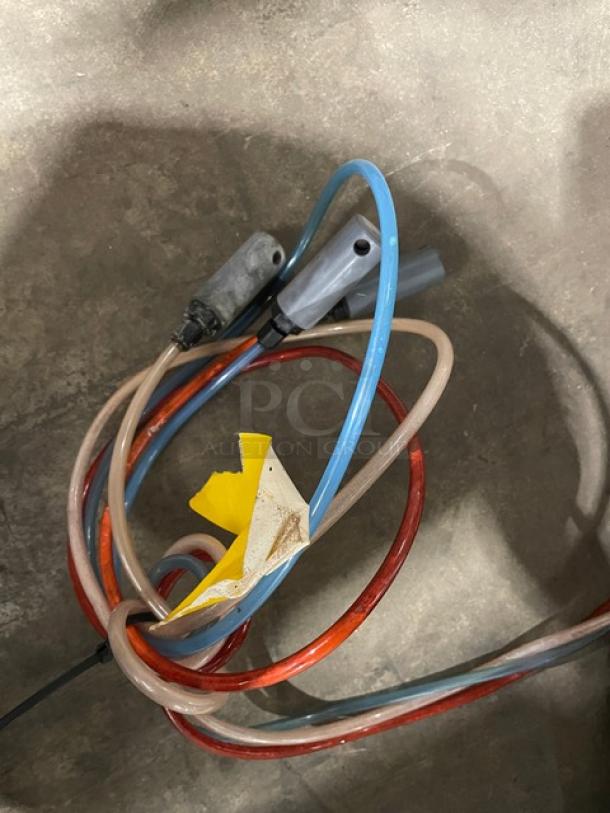 A coiled bundle of red, blue, and beige hoses with two connectors, set against a concrete background.