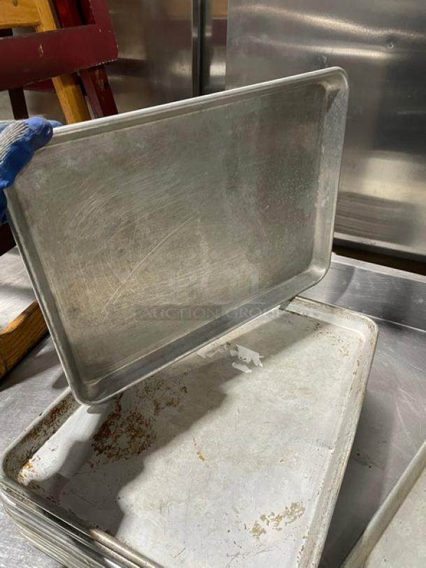 Commercial aluminum baking sheet pan, stack of seven, used condition with visible wear, ideal for bulk bidding.