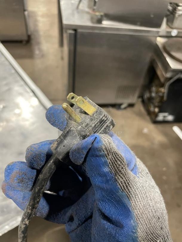 A gloved hand holding a power plug. Silver King SK48G commercial freezer in the background.