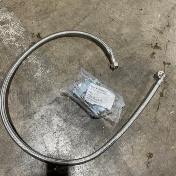 CMA undercounter dishwasher installation parts, including a flexible stainless steel hose and a bag of screws, on concrete floor.