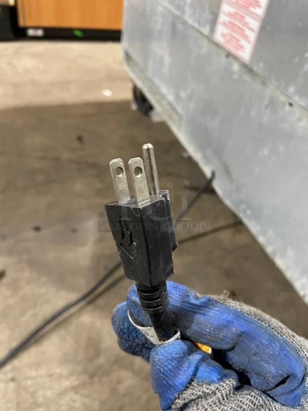 Power plug of a commercial stainless steel refrigerated prep table, held by a gloved hand, showcasing electrical compatibility.