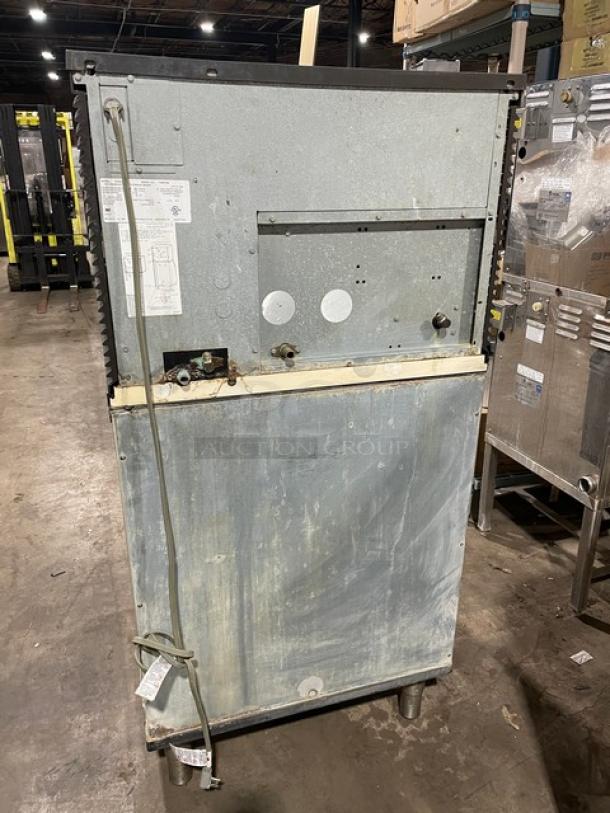 Manitowoc stainless steel ice maker/bin combo with lift-open access, electric-powered, on legs, visible tags affixed.