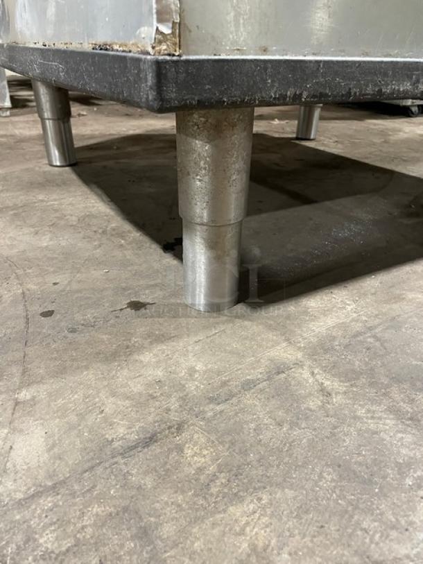 Manitowoc stainless steel ice making machine leg detail, showing slightly worn condition on a concrete floor.