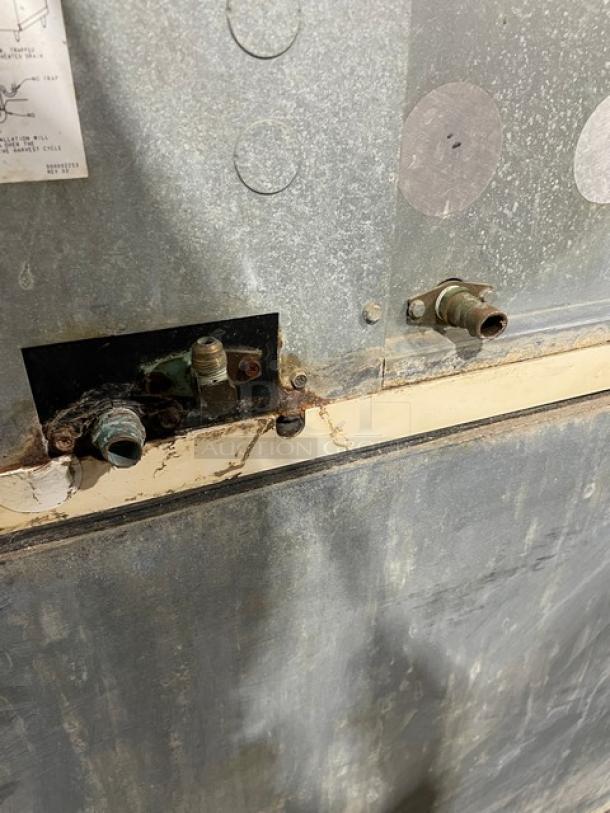 Manitowoc commercial stainless steel ice machine detail, showing the back panel with pipe connections and visible wear.