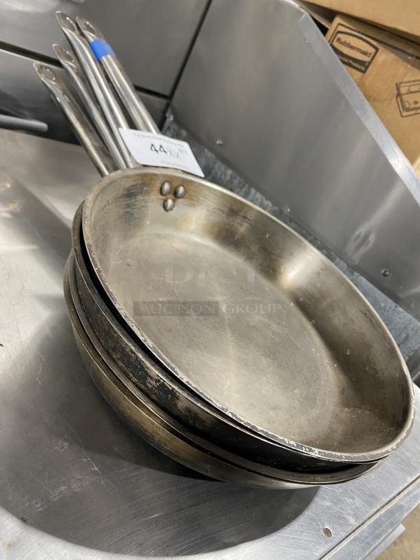 Stack of commercial round frying pans with riveted handles, visible wear, auction tag indicating "4X Your Bid!"