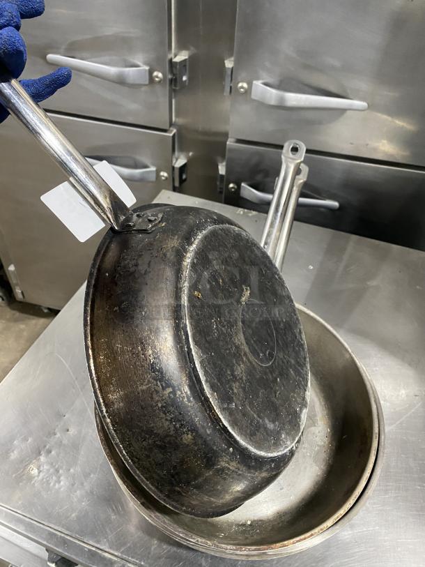 Commercial round frying pan, used condition, sturdy metal construction, visible wear on surface, attached label on handle.